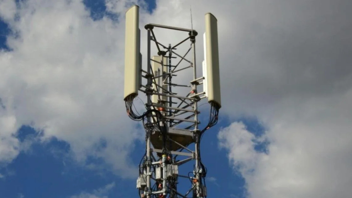 Cell tower with multiple antennas mounted on metal frame under cloudy sky