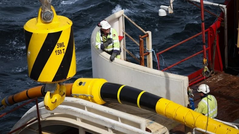 Engineers handling subsea cable component on deck