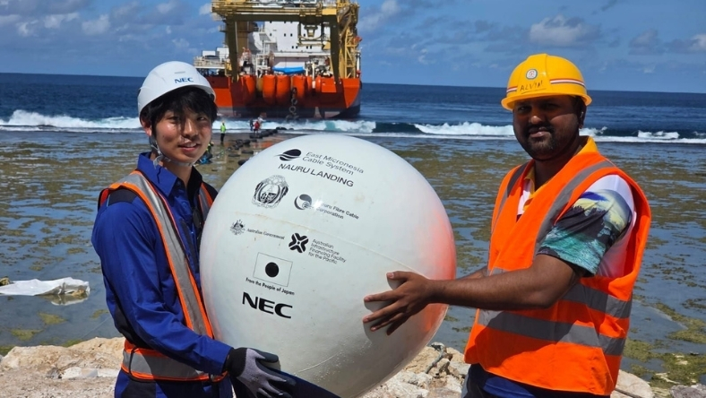 Technicians holding subsea cable landing sphere on beach with cable vessel offshore